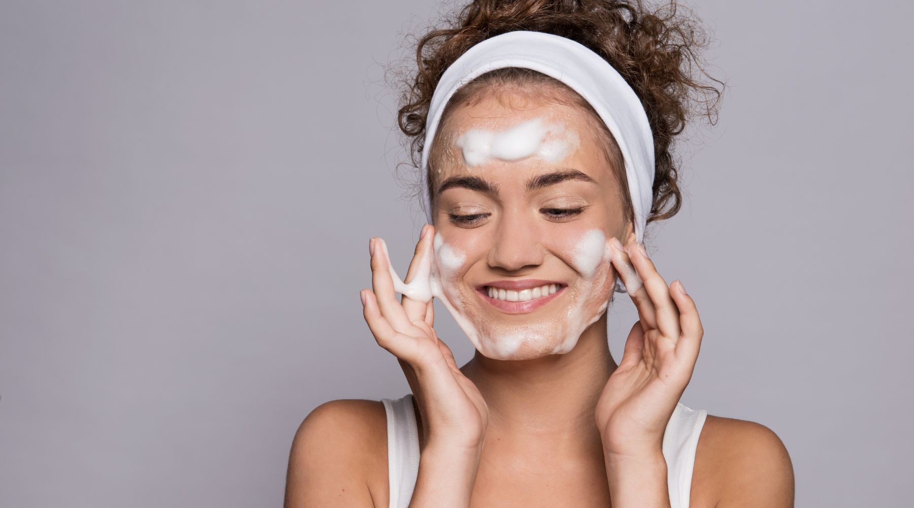 woman with headband on to keep her hair off her face, applying a foaming cleanser to her cheeks and forehead